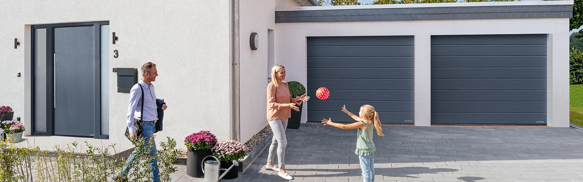 Frau und Kind spielen mit Ball vor Garage